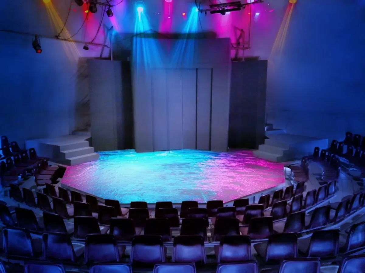 La sala de la Nueva Carpa Geodésica iluminada en azul, con el escenario al centro y las butacas alrededor